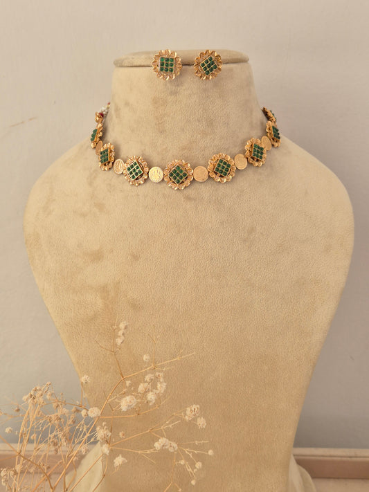 Gold-toned choker necklace and matching stud earrings set with circular floral-patterned motifs inlaid with emerald green stones by naitri.in