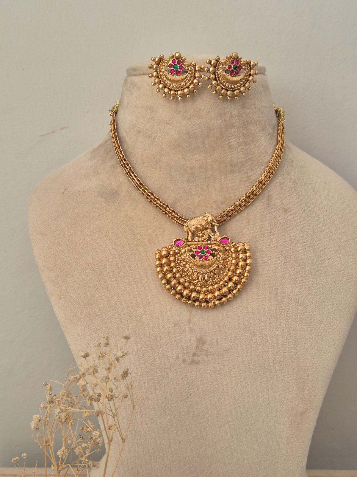 Gold temple necklace set with an elephant pendant, pink stone highlights, and matching stud earrings by naitri.in