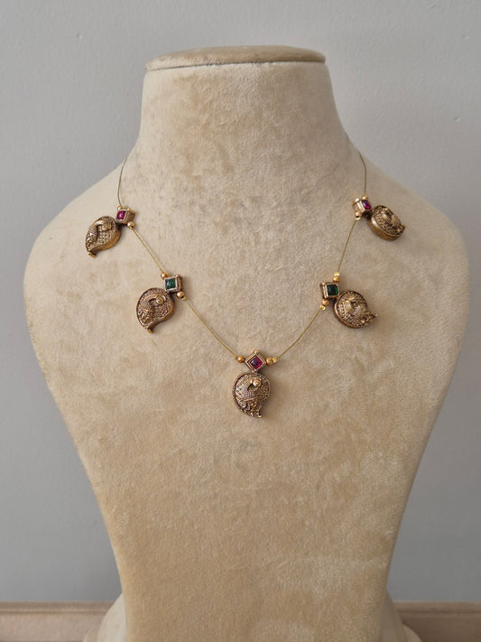  A minimalist gold-plated necklace featuring five peacock-themed pendants with red and green stone accents by naitri.in