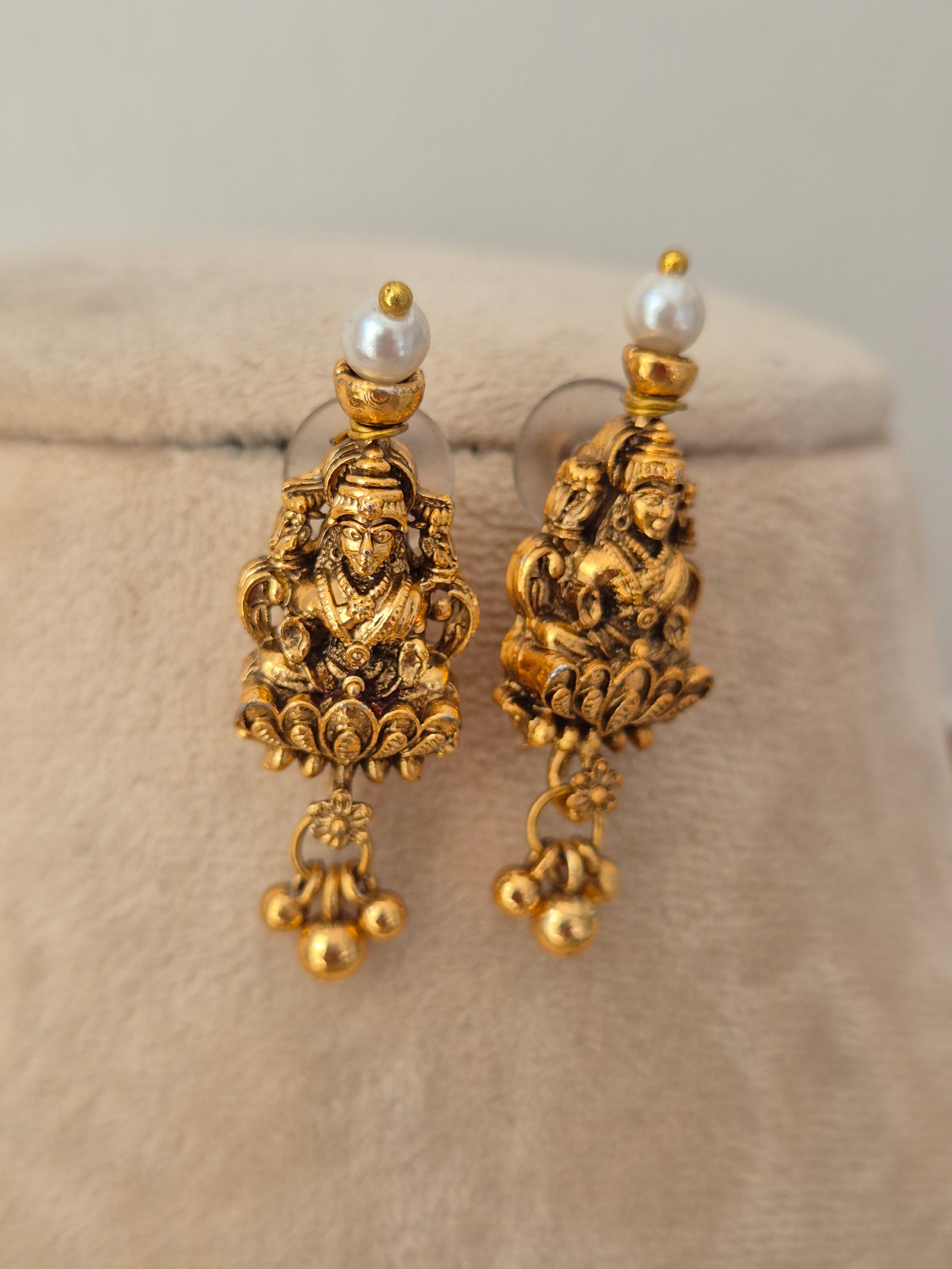 A pair of ornate gold-toned dangle earrings with detailed filigree work and a small white pearl at the top, by naitri.in