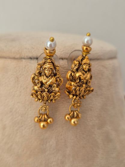 A pair of ornate gold-toned dangle earrings with detailed filigree work and a small white pearl at the top, by naitri.in