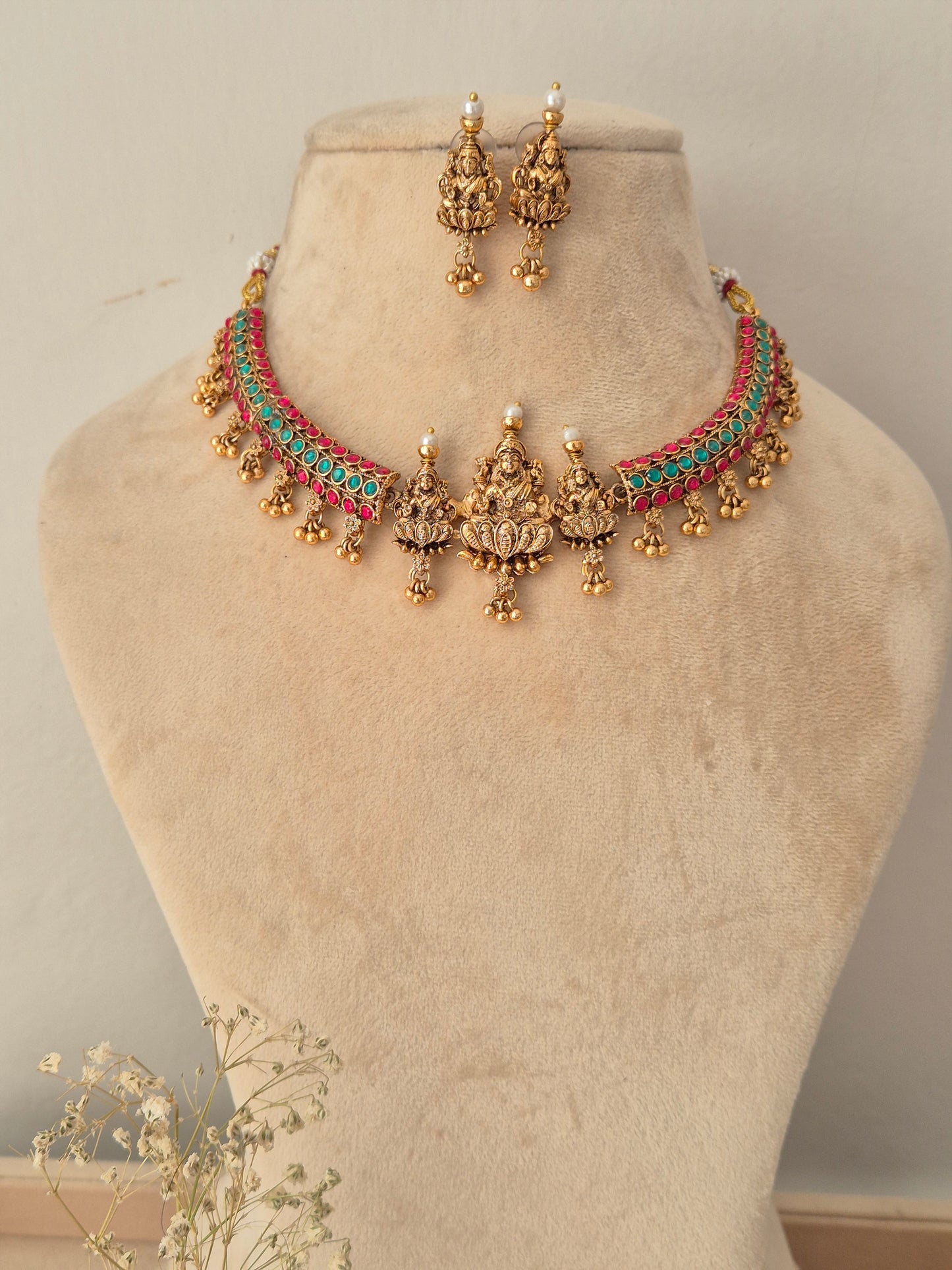 A traditional Indian jewelry set featuring a gold-plated choker necklace with turquoise and coral-red woven accents, matching drop earrings, by naitri.in