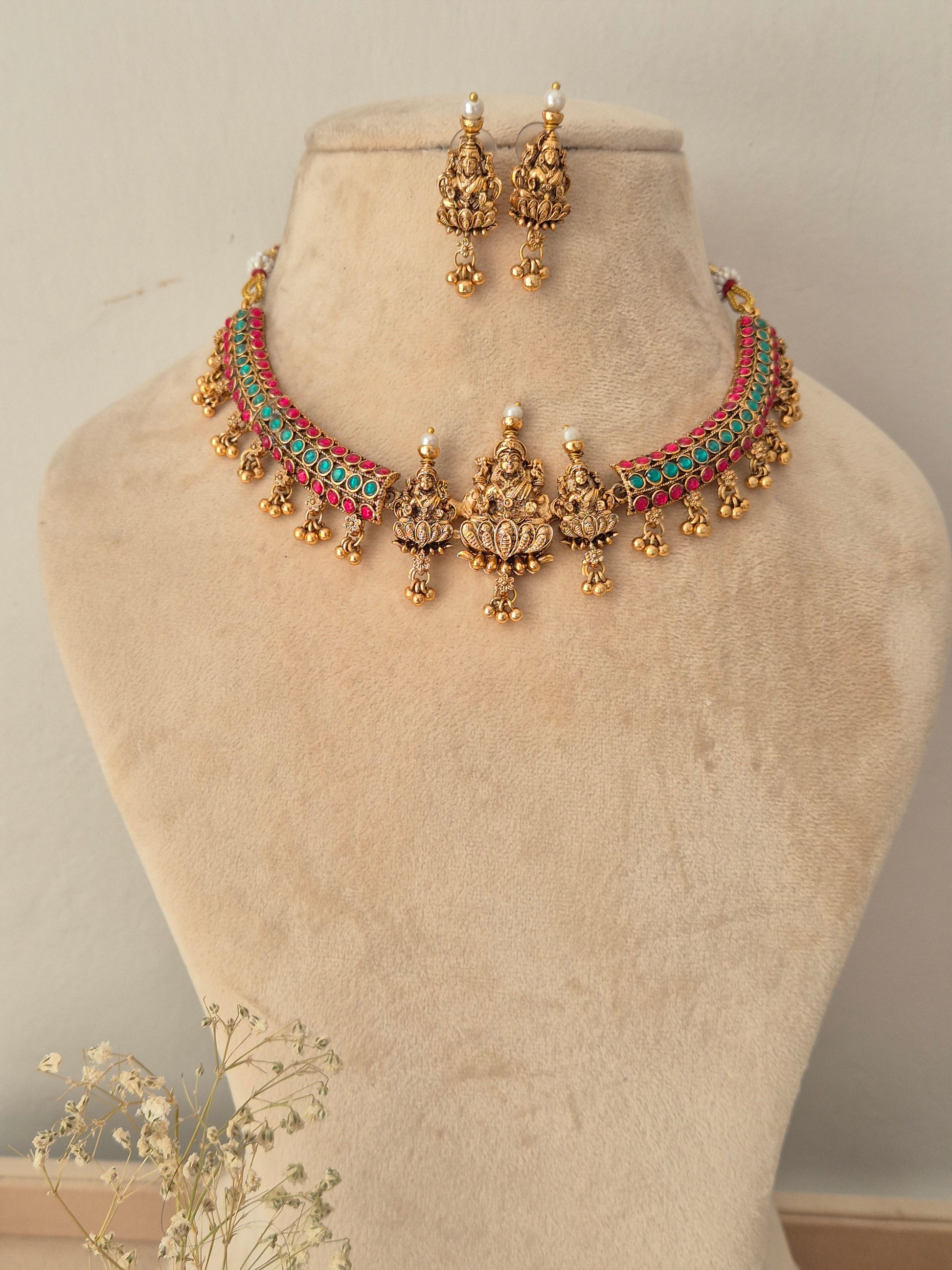 A traditional Indian jewelry set featuring a gold-plated choker necklace with turquoise and coral-red woven accents, matching drop earrings, by naitri.in