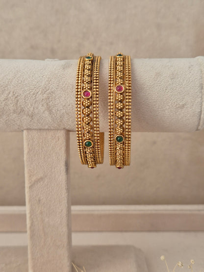 Set of 2 gold-plated bangles decorated with intricate floral beadwork, studded with small pink and green gemstones by naitri.in