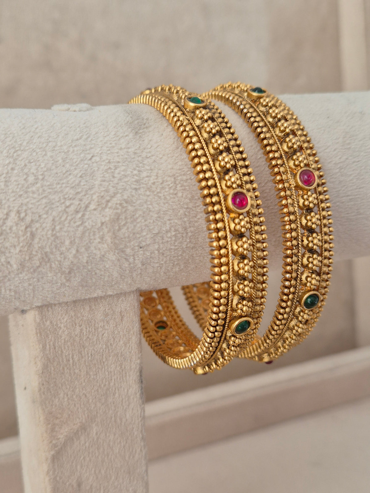 Festive Indian gold-plated bangles featuring delicate floral relief patterns and colorful gemstone accents for weddings and special occasions by naitri.in