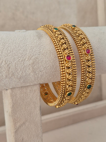 Festive Indian gold-plated bangles featuring delicate floral relief patterns and colorful gemstone accents for weddings and special occasions by naitri.in