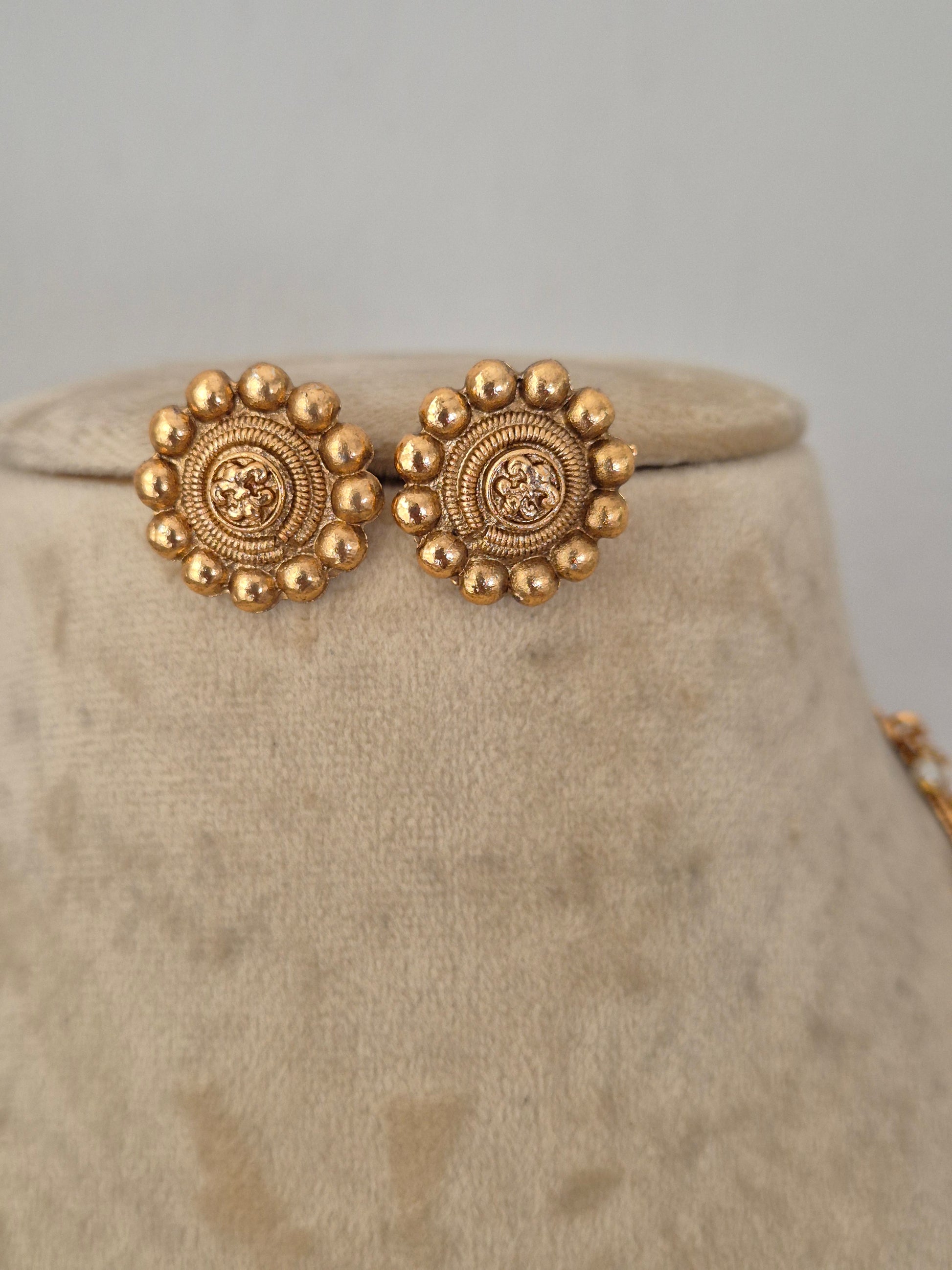 A close-up of ornate gold-toned detailed and circular earrings by naitri.in