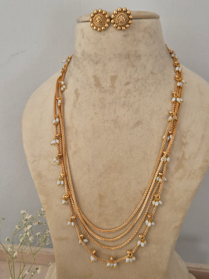 A gold-toned multi-strand necklace with small white pearl-like bead accents, a matching round gold stud earring by naitri.in