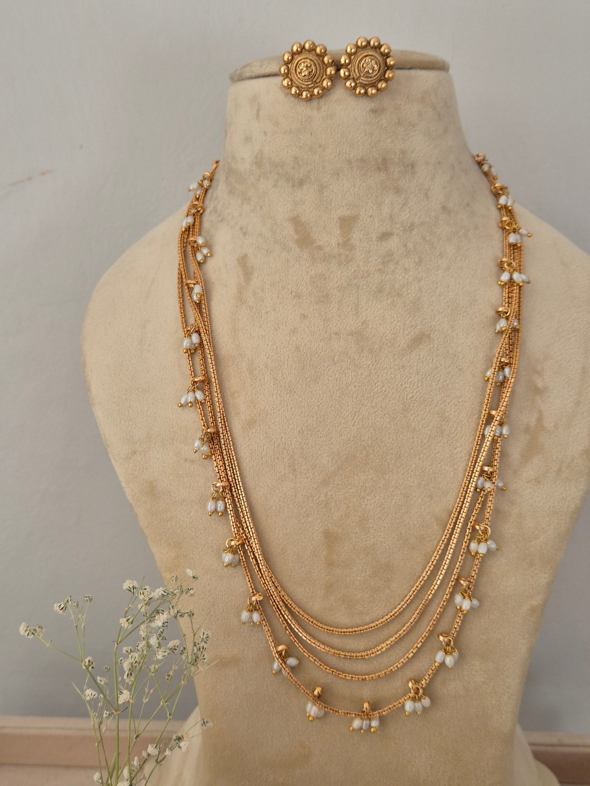 A gold-toned multi-strand chain necklace with small white pearl-like beads, a matching gold-toned circular pendant by naitri.in