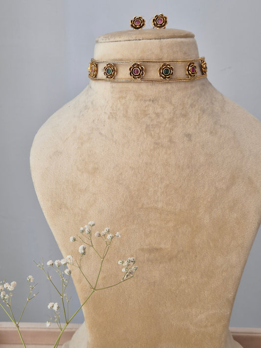 A handcrafted gold-plated brass choker with circular floral motifs, featuring pink and green stone centers and matching stud earrings by naitri.in