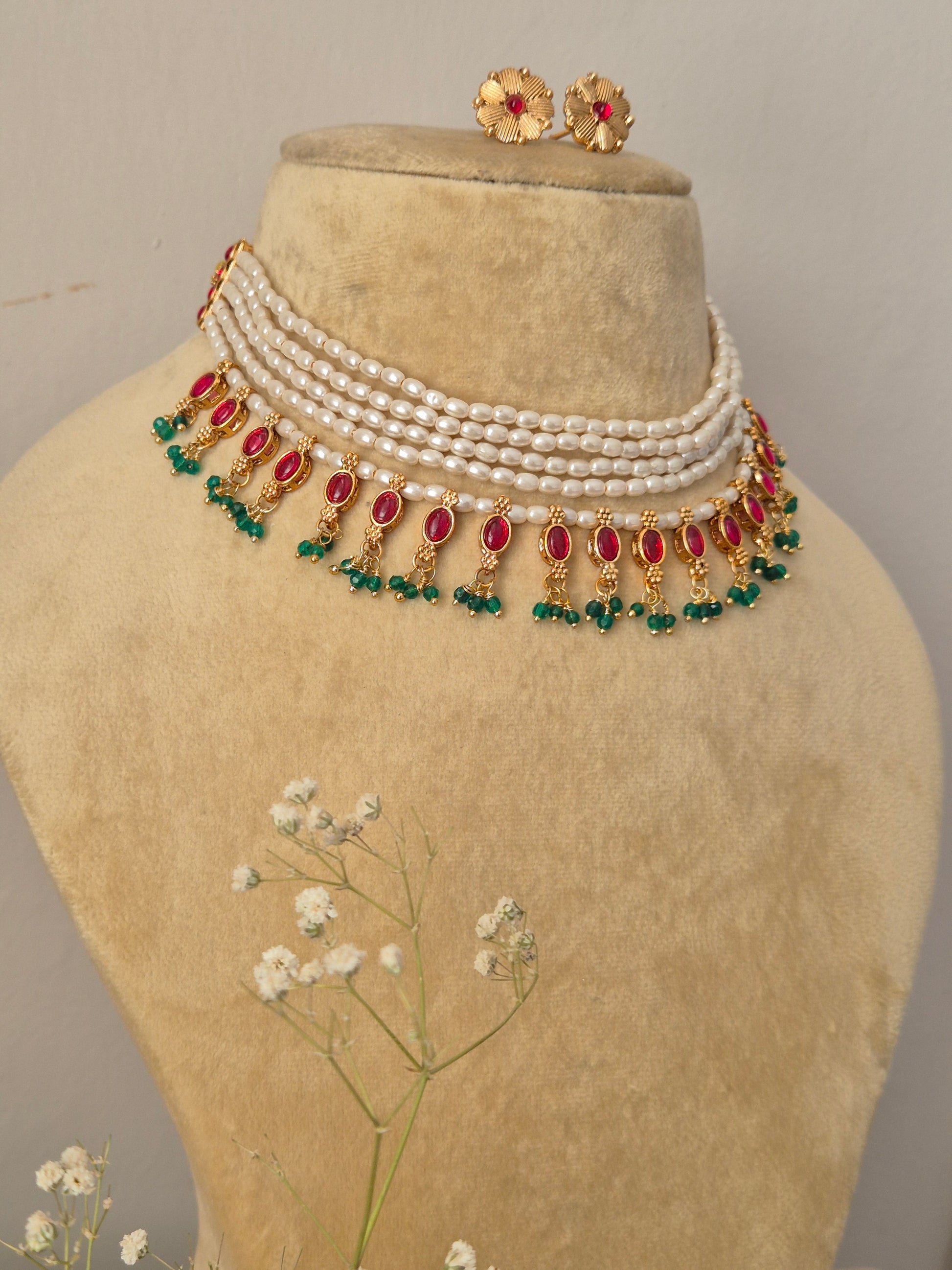 Artisanal Rashmi pearl necklace and earring set styled on a neutral cream display bust with a delicate sprig of white baby's breath flowers